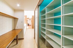 キッチンの並びにワークデスク、その対面に引戸がついたパントリー、撮影者の背面が脱衣ランドリー室、という一直線の家事動線になっている。