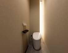 トイレの右奥の角を間接照明と収納を兼ねたスペースとした。収納の棚が奥まっているので直接見えず、すっきりとした印象になっている。
