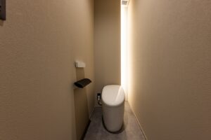 トイレの右奥の角を間接照明と収納を兼ねたスペースとした。収納の棚が奥まっているので直接見えず、すっきりとした印象になっている。